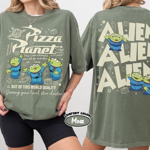 May include: Olive green t-shirt featuring the Pizza Planet logo and cartoon aliens. The front of the shirt has the text "Pizza Planet" and "Out of this world quality". The back of the shirt has the word "ALIEN" repeated three times with cartoon aliens.