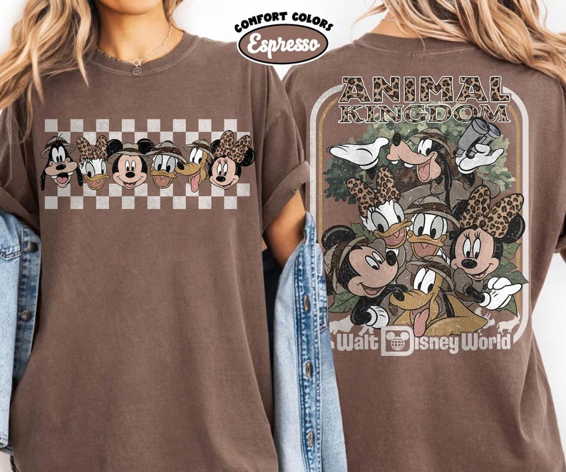 K&ouml;nnte beinhalten: Espressofarbenes T-Shirt mit einer Grafik von Disney-Charakteren. Die Vorderseite zeigt Gesichter von Charakteren auf einem Schachbrettmuster. Die R&uuml;ckseite hat ein Animal Kingdom-Design mit Charakteren und dem Text "Walt Disney World".