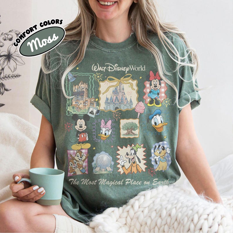 May include: Moss green t-shirt featuring a Walt Disney World design with various cartoon characters and park icons. The shirt includes the text "The Most Magical Place on Earth" and "Comfort Colors".