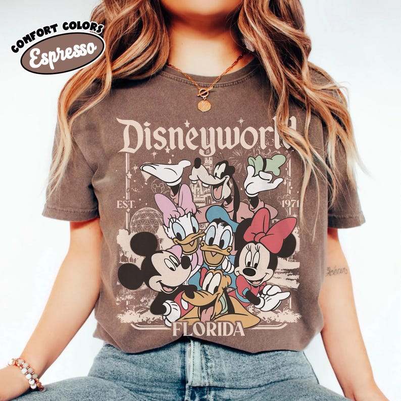 May include: Espresso-colored t-shirt featuring a vintage-style Disney World graphic. The design includes Mickey Mouse, Minnie Mouse, Donald Duck, Daisy Duck, Goofy, and other characters. The text "Disneyworld Florida" is displayed prominently.
