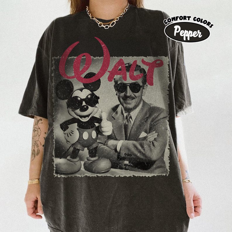 K&ouml;nnte beinhalten: Dunkelgraues T-Shirt mit einem Vintage-Grafik von Mickey Mouse und Walt Disney mit Sonnenbrille. Das Wort "WALT" ist rot &uuml;ber dem Bild gedruckt. Das Shirt hat auch die Worte "COMFORT COLORS" und "Pepper" aufgedruckt.
