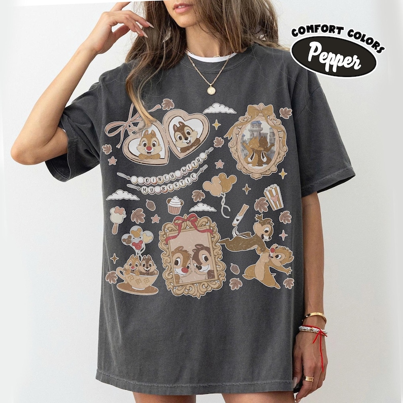 May include: Dark gray Comfort Colors t-shirt featuring Chip and Dale cartoon graphics in ornate frames, hearts, and clouds. The shirt includes the text "Dooney & Bourke" and "Comfort Colors Pepper".
