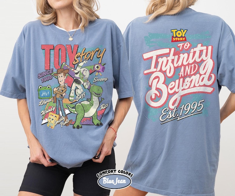 Pode incluir: Uma t-shirt azul com gr&aacute;ficos de Toy Story. A frente mostra Woody, Buzz Lightyear, Rex e Smarty Pants com texto incluindo Toy Story, Since 1995, Hi, Lilypad, Snappy e Woody. As costas apresentam o texto To Infinity and Beyond Est. 1995.