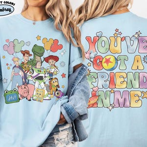 May include: A light blue t-shirt featuring a front graphic of Toy Story characters including Woody, Buzz Lightyear, Jessie, Rex, and Hamm with balloons. The back graphic displays the colourful text "YOU'VE GOT A FRIEND IN ME" with stars.