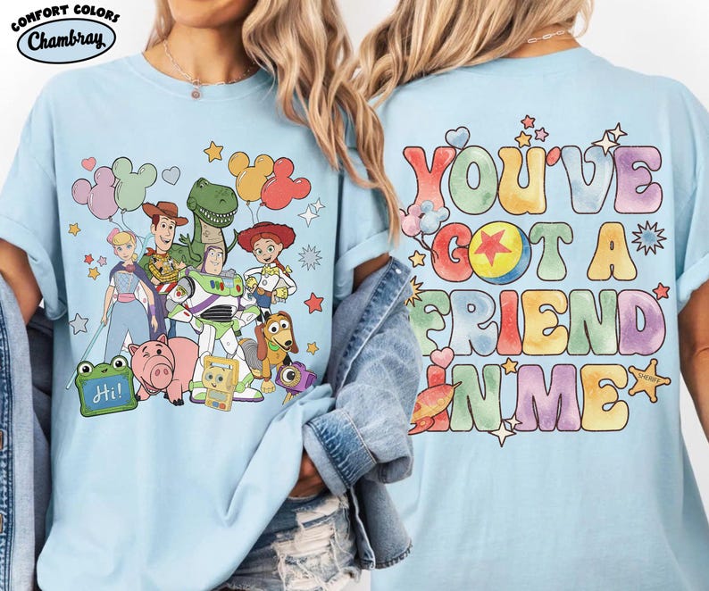 May include: A light blue t-shirt featuring a front graphic of Toy Story characters including Woody, Buzz Lightyear, Jessie, Rex, and Hamm with balloons. The back graphic displays the colourful text "YOU'VE GOT A FRIEND IN ME" with stars.