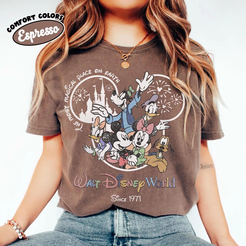 May include: Espresso-colored t-shirt featuring a graphic of Disney characters including Mickey Mouse, Minnie Mouse, Donald Duck, Daisy Duck, Goofy, and Pluto. The design includes the text "The Most Magical Place on Earth" and "Walt Disney World Since 1971."