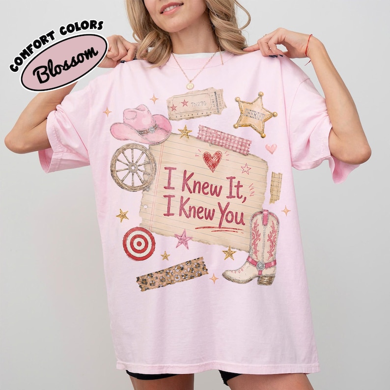 Puede incluir: Una camiseta rosa claro con un estampado gr&aacute;fico de un sombrero de vaquero, una rueda de carreta, una estrella de sheriff, una diana y una bota vaquera. En el centro, una nota de papel rayado muestra el texto I Knew It, I Knew You y un coraz&oacute;n rojo.