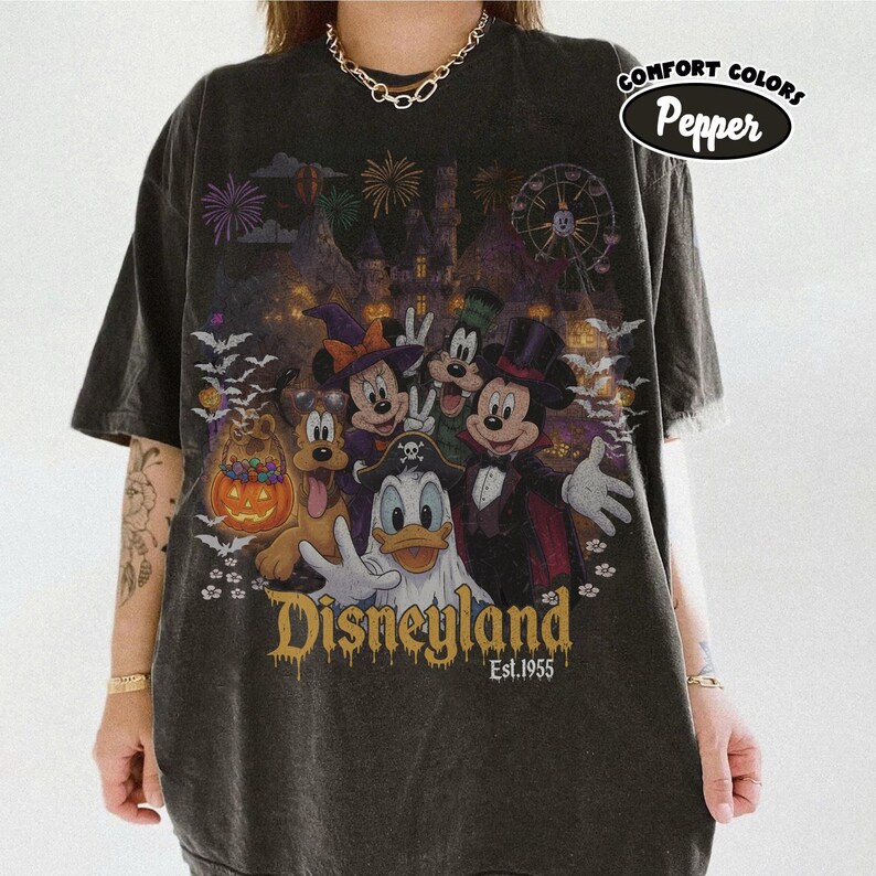 May include: A charcoal gray t-shirt featuring a graphic of Disney characters in Halloween costumes, including Mickey Mouse, Minnie Mouse, Donald Duck, Goofy, and Pluto. The design includes a pumpkin, bats, fireworks, and the text Disneyland Est. 1955.