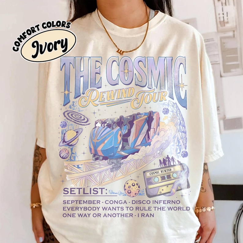 K&ouml;nnte beinhalten: Elfenbeinfarbenes T-Shirt mit einem Grafikdesign, das f&uuml;r "The Cosmic Rewind Tour" wirbt. Das Design zeigt eine Achterbahn, Planeten und die Aufschrift "SETLIST:" mit Songtiteln. Das Shirt hat auch die Worte "COMFORT COLORS" und "Ivory" in einem Kreis.