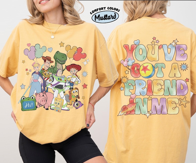 May include: A mustard yellow t-shirt featuring a front graphic of Toy Story characters including Woody, Buzz Lightyear, and Jessie with balloons. The back graphic displays the text "YOU'VE GOT A FRIEND IN ME" in colourful bubble letters with a rocket.