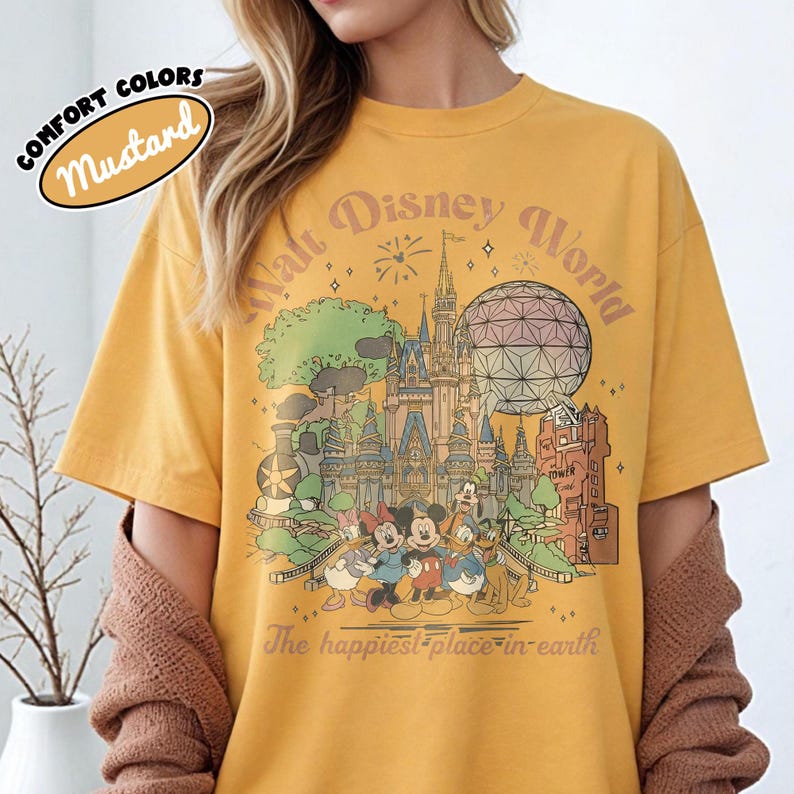 May include: Mustard-colored t-shirt featuring a colorful graphic of Disney World with Mickey Mouse, Minnie Mouse, Donald Duck, and Goofy. The text on the shirt reads "Walt Disney World" and "The happiest place on earth."