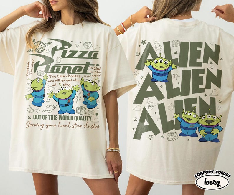 May include: Ivory-colored t-shirt featuring the Pizza Planet logo and three green aliens on the front. The back of the shirt displays the word "ALIEN" three times with the same aliens. The shirt has the text "OUT OF THIS WORLD QUALITY" and "Serving your local star cluster".