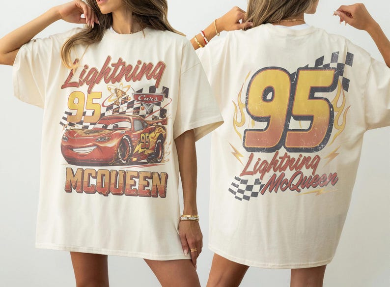 Może przedstawiać: Kremowa koszulka z grafiką Zygzaka McQueena z filmu Auta. Prz&oacute;d przedstawia postać z napisem "Lightning 95 McQueen". Tył ma duży napis "95" i "Lightning McQueen" z płomieniami i szachownicą.
