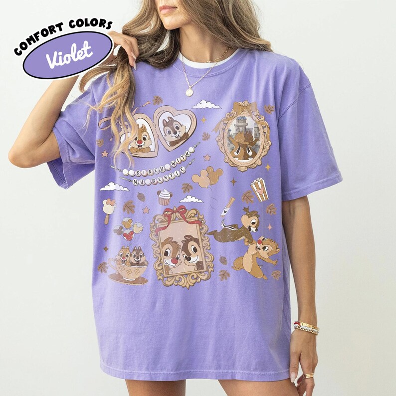 May include: Violet Comfort Colors t-shirt featuring cartoon characters in ornate frames and decorative elements. The shirt has a relaxed fit and a crew neck. The text "Comfort Colors" and "Violet" are in a bubble on the top left.