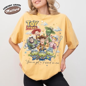 May include: Mustard yellow t-shirt with a graphic of characters from the film "Toy Story." The design includes Woody, Buzz Lightyear, and other characters, with the text "You've got a Friend in me."