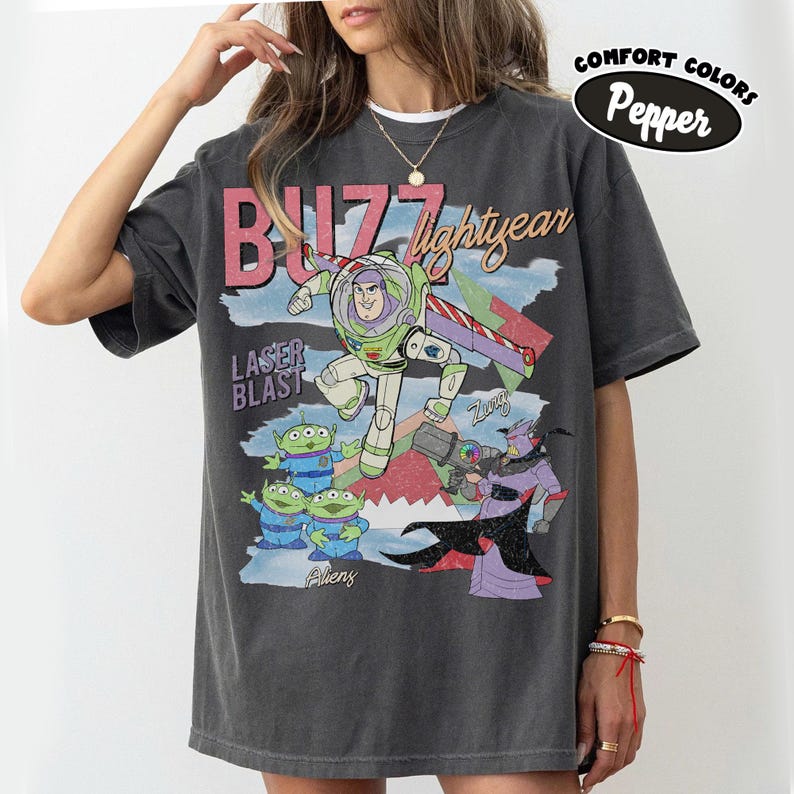 May include: Dark grey t-shirt with a graphic of Buzz Lightyear from Toy Story. The design includes the text "Buzz Lightyear" and "Laser Blast", plus images of aliens and Zurg. The shirt has a vintage, distressed appearance.