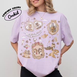 May include: Orchid-colored t-shirt with cartoon graphics of Chip and Dale, framed portraits, and food icons. The shirt features the text "COMFORT COLORS" and "Orchid" in a circular design. The design includes hearts, clouds, and stars.
