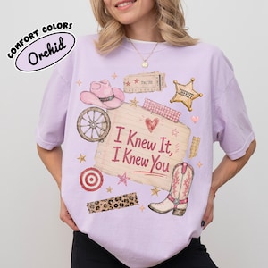 Puede incluir: Una camiseta de color morado claro con un estampado gr&aacute;fico de un sombrero de vaquero rosa, una rueda de carreta, una estrella de sheriff, una diana roja, una tira de estampado de leopardo y una bota. El centro muestra una nota con I Knew It, I Knew You.