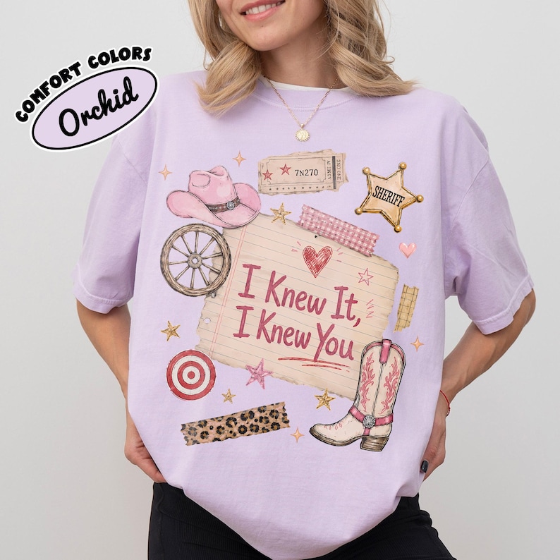 Puede incluir: Una camiseta de color morado claro con un estampado gr&aacute;fico de un sombrero de vaquero rosa, una rueda de carreta, una estrella de sheriff, una diana roja, una tira de estampado de leopardo y una bota. El centro muestra una nota con I Knew It, I Knew You.