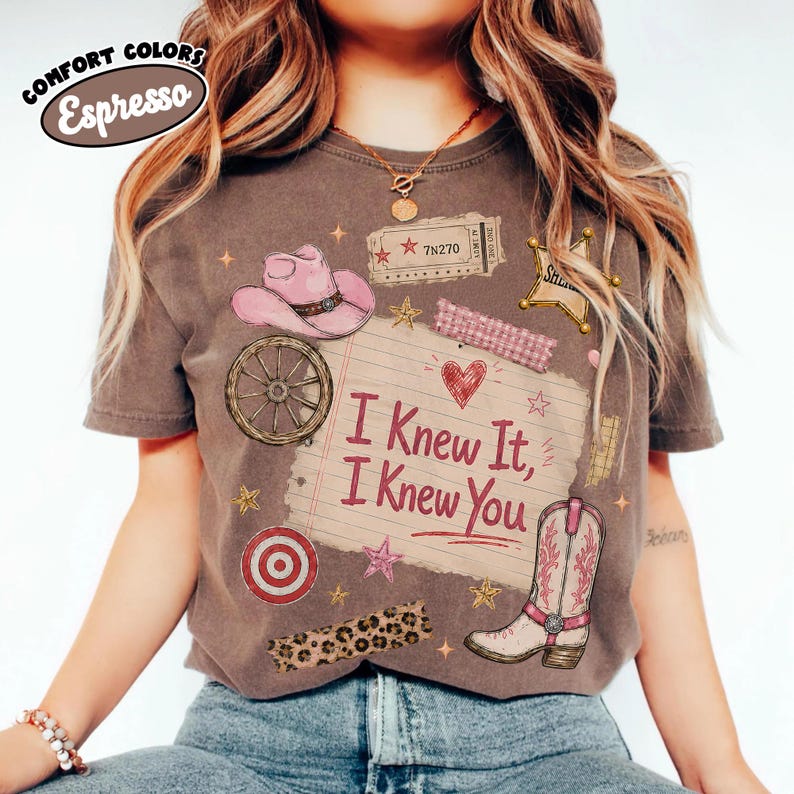 Puede incluir: Una camiseta marr&oacute;n de manga corta con un estampado gr&aacute;fico de un sombrero de vaquero rosa, una rueda de carreta, una estrella de sheriff, una diana y una bota de vaquero. El centro muestra una nota con l&iacute;neas y el texto I Knew It, I Knew You.