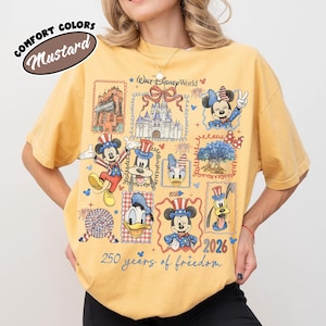 May include: Mustard-colored t-shirt featuring a collage of Disney characters and landmarks, including Mickey Mouse, Minnie Mouse, and Cinderella's castle. The shirt has the text "Walt Disney World" and "250 years of freedom 2026".