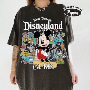 Op de afbeelding: Een antracietgrijs t-shirt met korte mouwen en een afbeelding van Mickey Mouse boven de tekst Est. 1955. Het ontwerp bevat kleurrijke illustraties van Disneyland-attracties en de tekst Walt Disney's Disneyland. Comfort Colors Pepper.