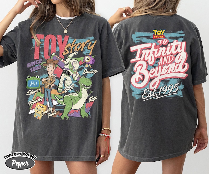 Pode incluir: Uma camiseta de manga curta cinza-carv&atilde;o com gr&aacute;ficos de Toy Story. A frente exibe Woody, Buzz Lightyear, Rex e texto incluindo "Toy Story" e "Since 1995". As costas apresentam o texto "Toy Story To Infinity and Beyond Est. 1995".
