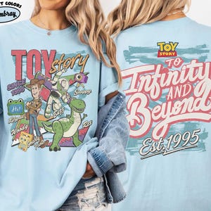 Pode incluir: Uma t-shirt azul claro com gr&aacute;ficos de Toy Story. A frente mostra Woody, Buzz Lightyear, Rex e outras personagens com o texto "Toy Story Since 1995". As costas apresentam o log&oacute;tipo de Toy Story e o texto "To Infinity and Beyond Est. 1995".