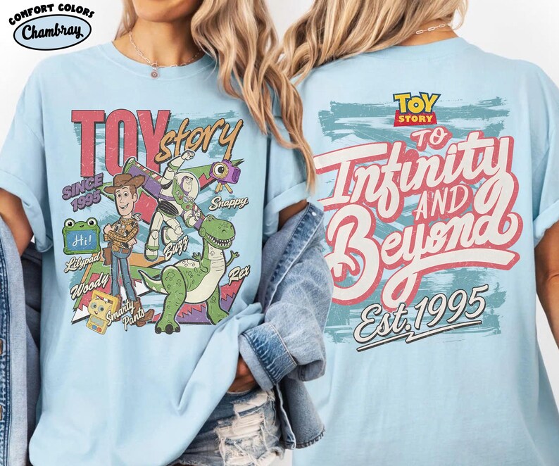 Pode incluir: Uma t-shirt azul claro com gr&aacute;ficos de Toy Story. A frente mostra Woody, Buzz Lightyear, Rex e outras personagens com o texto "Toy Story Since 1995". As costas apresentam o log&oacute;tipo de Toy Story e o texto "To Infinity and Beyond Est. 1995".