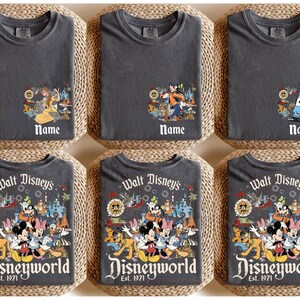 May include: Six charcoal gray t-shirts with Disney character graphics. Three shirts have a character graphic with the word "Name" below. The other three shirts have a Disneyworld graphic with "Est. 1971".