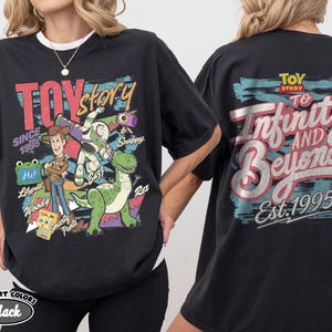 Pode incluir: Uma t-shirt preta com gr&aacute;ficos de Toy Story. A frente mostra Woody, Buzz Lightyear, Rex e outras personagens com texto incluindo "TOY story", "SINCE 1995" e nomes. As costas apresentam "TOY STORY" e "To Infinity AND Beyond Est. 1995."