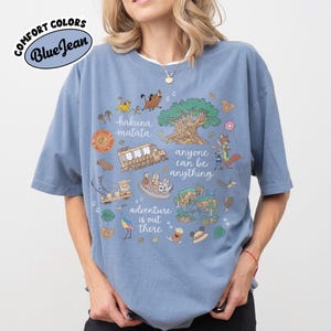 Puede incluir: Camiseta azul Comfort Colors con un dise&ntilde;o gr&aacute;fico que presenta los textos "hakuna matata", "anyone can be anything" y "adventure is out there". El dise&ntilde;o incluye ilustraciones de dibujos animados de animales y un &aacute;rbol.