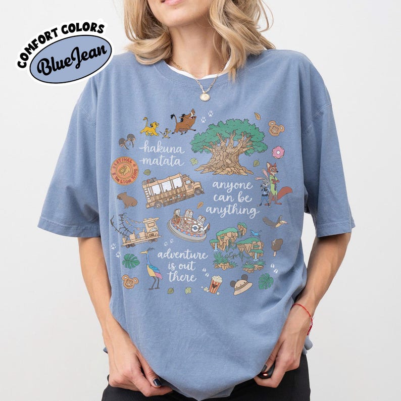 Puede incluir: Camiseta azul Comfort Colors con un dise&ntilde;o gr&aacute;fico que presenta los textos "hakuna matata", "anyone can be anything" y "adventure is out there". El dise&ntilde;o incluye ilustraciones de dibujos animados de animales y un &aacute;rbol.