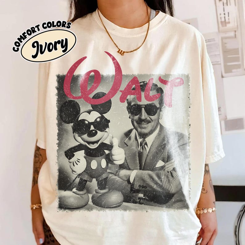 K&ouml;nnte beinhalten: Elfenbeinfarbenes T-Shirt mit einem Retro-Grafikdesign von Mickey Mouse und Walt Disney, beide mit Sonnenbrille. Das Wort "WALT" ist in Rosa &uuml;ber dem Bild gedruckt. Das Shirt hat auch die Aufschrift "COMFORT COLORS" und "Ivory".