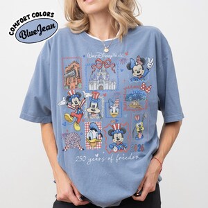 May include: Blue Comfort Colors t-shirt with a Disney World graphic. The graphic includes images of Mickey Mouse, Minnie Mouse, Donald Duck, and Goofy, along with the text "250 years of freedom" and "2026".
