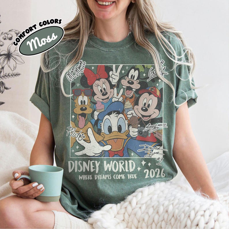 May include: Moss green t-shirt featuring a Disney World graphic with Mickey Mouse, Minnie Mouse, Donald Duck, and other characters. The shirt includes the text "Disney World Where Dreams Come True 2026".