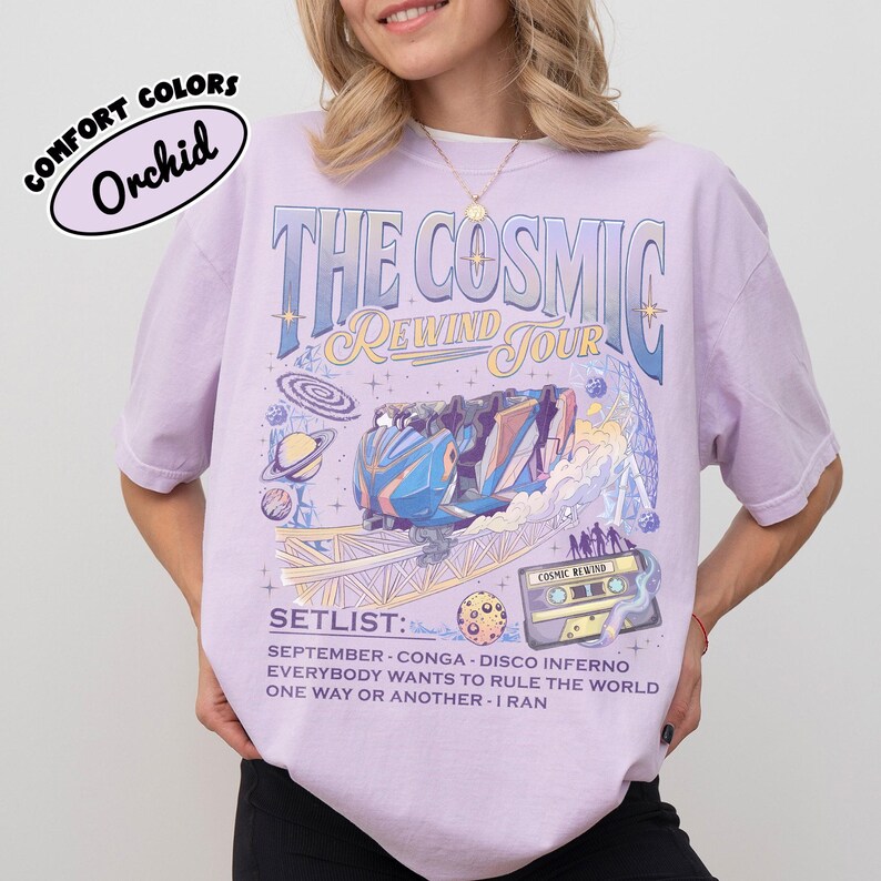 K&ouml;nnte beinhalten: Ein helllila T-Shirt mit einem grafischen Design mit dem Text "THE COSMIC REWIND TOUR". Das Design umfasst eine Achterbahn, Planeten und eine Kassette. Das Shirt listet auch eine Setlist auf.