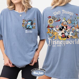 May include: A blue Comfort Colors t-shirt featuring a Disney theme. The front has a cartoon car design with the word "Name" below it. The back displays a colorful Disney World graphic with the text "Walt Disney's Disneyworld Est. 1971".