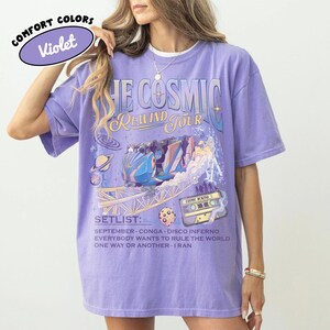 K&ouml;nnte beinhalten: Violettes Comfort Colors T-Shirt mit "THE COSMIC REWIND TOUR" Grafik. Das Design umfasst eine Achterbahn, Planeten und eine Kassette. Die Setlist enth&auml;lt "September", "Conga" und "Disco Inferno".