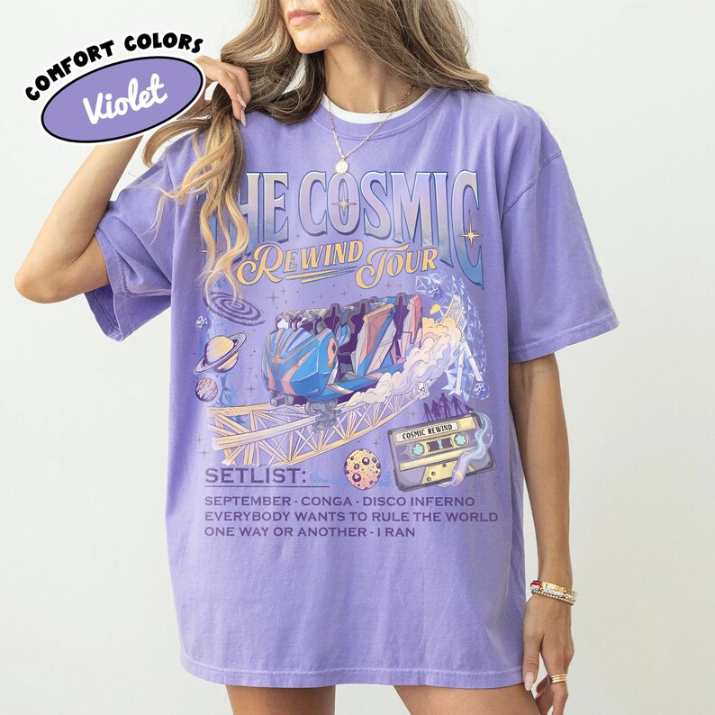 K&ouml;nnte beinhalten: Violettes Comfort Colors T-Shirt mit "THE COSMIC REWIND TOUR" Grafik. Das Design umfasst eine Achterbahn, Planeten und eine Kassette. Die Setlist enth&auml;lt "September", "Conga" und "Disco Inferno".