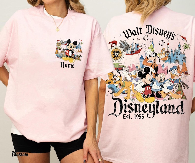 Peut inclure: T-shirt rose clair avec des motifs de Mickey Mouse et Disneyland. Le devant pr&eacute;sente un petit motif de Mickey Mouse avec le mot "Name" en dessous. Le dos affiche une grande sc&egrave;ne de Disneyland avec divers personnages Disney.