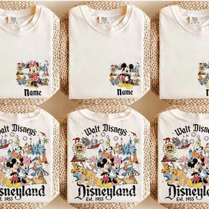 Peut inclure: Six t-shirts blancs avec des graphiques de personnages Disney. Les chemises pr&eacute;sentent des motifs de Mickey Mouse, Minnie Mouse et Simba, ainsi qu'un graphique Disneyland. Le texte "Name" appara&icirc;t sous les images des personnages. Les chemises du bas affichent "Walt Disney's Disneyland Est. 1955".