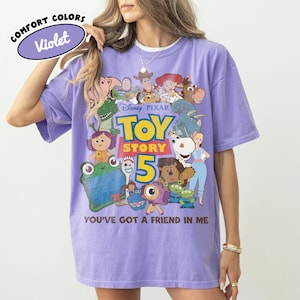 Op de afbeelding: Een violetkleurig T-shirt met korte mouwen en een grafische print van diverse Toy Story-personages. Het ontwerp bevat de tekst Disney Pixar Toy Story 5 en de zin You've Got A Friend In Me. Een klein ovaal label toont Comfort Colors Violet.