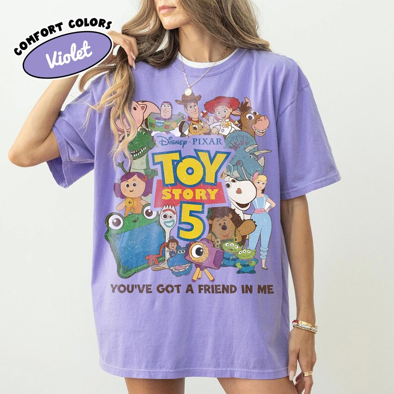 Op de afbeelding: Een violetkleurig T-shirt met korte mouwen en een grafische print van diverse Toy Story-personages. Het ontwerp bevat de tekst Disney Pixar Toy Story 5 en de zin You've Got A Friend In Me. Een klein ovaal label toont Comfort Colors Violet.