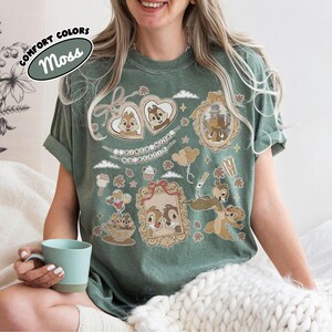 May include: Moss green t-shirt featuring Chip and Dale cartoon graphics in heart-shaped frames and other decorative elements. The shirt includes the text "Comfort Colors" and "Moss". The design is a playful and nostalgic tribute to the beloved characters.