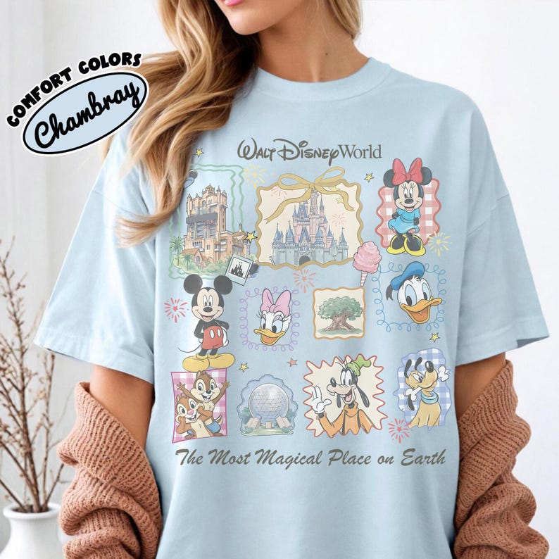 May include: Light blue t-shirt with a Walt Disney World graphic. The design includes various Disney characters and park icons within framed illustrations. The text "The Most Magical Place on Earth" is printed at the bottom. The shirt also has the text "Comfort Colors Chambray".