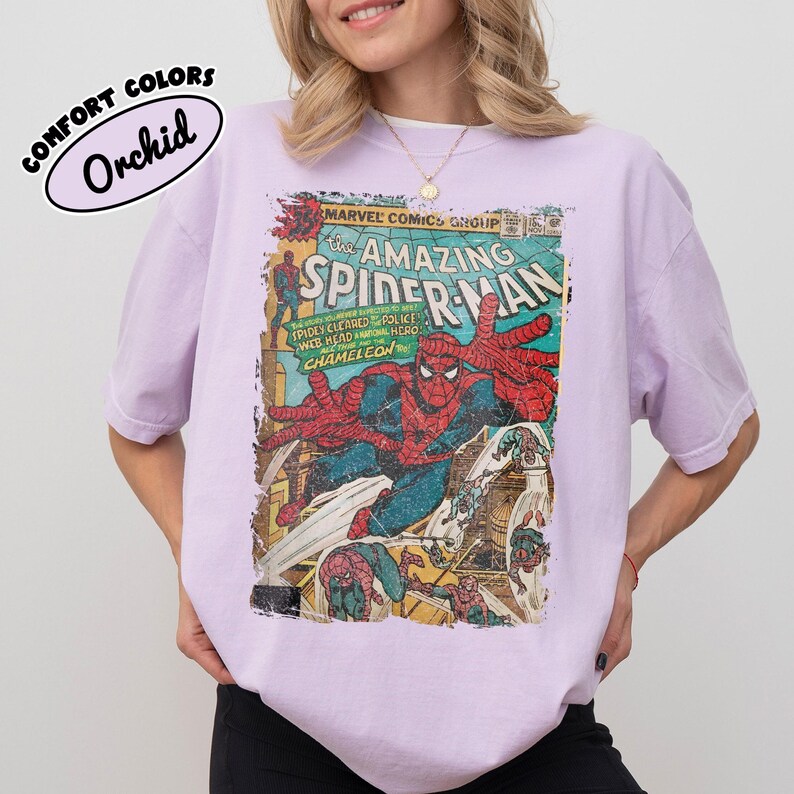 May include: A light purple t-shirt featuring a vintage-style Marvel Comics The Amazing Spider-Man graphic print on the front. The design includes Spider-Man in a red and blue suit, with text that reads The Amazing Spider-Man and Comfort Colors Orchid.