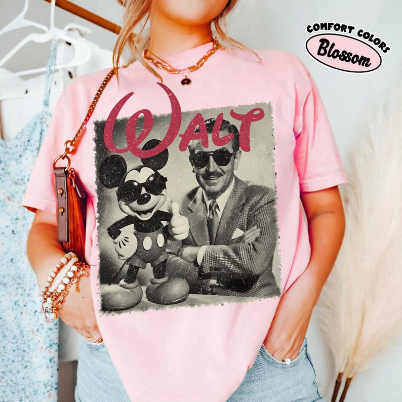 K&ouml;nnte beinhalten: Hellrosa T-Shirt mit einem Vintage-Grafik von Walt Disney und Mickey Mouse mit Sonnenbrille. Das Wort "Walt" ist in einem rosa Glitzer-Schriftzug gehalten. Das Shirt hat auch den Text "Comfort Colors Blossom".