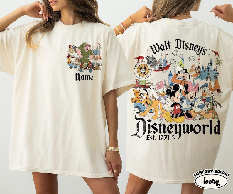 May include: Ivory-colored t-shirt featuring a Disney-themed graphic. The front displays a cartoon image with the text "Name". The back showcases Disney characters with "Walt Disney's Disneyworld Est. 1971".