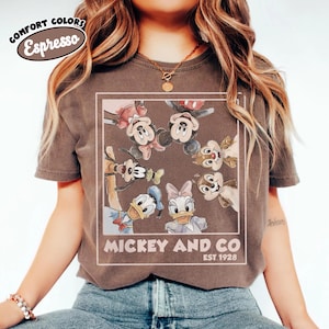 Puede incluir: Camiseta color espresso con un gr&aacute;fico enmarcado de Mickey Mouse, Minnie Mouse, Donald Duck, Daisy Duck, Goofy y Chip y Chop. El texto "Mickey and Co. EST. 1928" est&aacute; impreso debajo. La camiseta tiene mangas cortas.